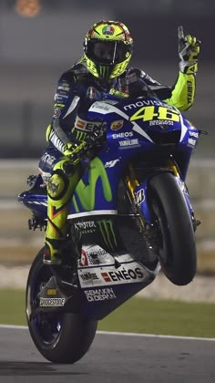 a man riding on the back of a blue and yellow motorcycle in front of a race track