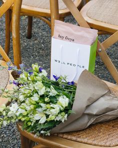 a bouquet of flowers sitting on top of a wooden chair next to a paper bag