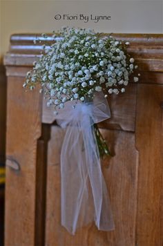 a bouquet of baby's breath tied to the side of a wooden church pew