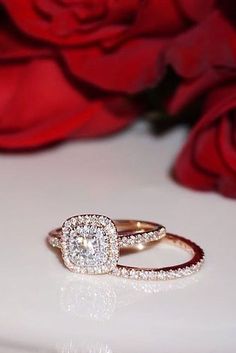 a diamond ring sitting on top of a white surface next to red roses and petals