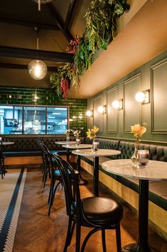 an empty restaurant with green walls and wooden tables, black chairs and plants hanging from the ceiling