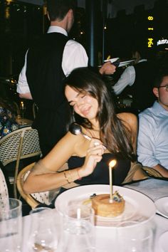 a woman sitting at a table with a cake and candle in front of her face