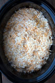 a crock pot filled with shredded cheese on top of a wooden table