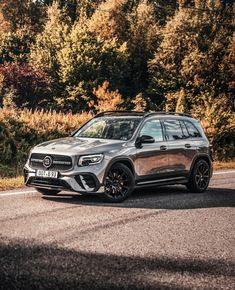 the new mercedes gle - class suv is driving on a road in front of some trees