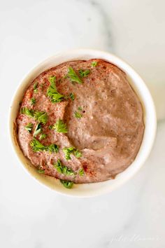 a white bowl filled with hummus and garnished with parsley on top