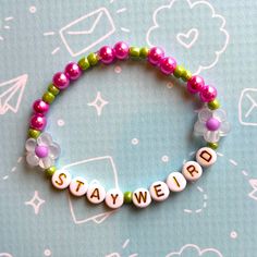 a beaded bracelet with the word stay weird written in white letters and pink beads