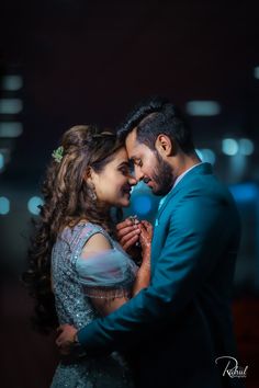 a man and woman embracing each other in front of a dark background with lights behind them