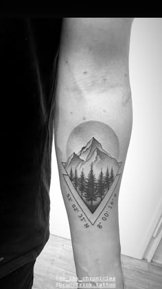 a man's arm with a mountain and pine tree tattoo on the left forearm