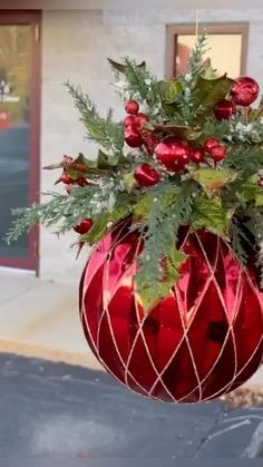 a red vase filled with greenery sitting on top of a parking lot next to a building