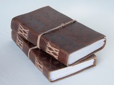 two brown books with white pages are stacked on top of each other and tied together