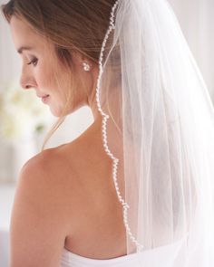 a woman wearing a wedding veil with pearls on the back of her head and shoulder