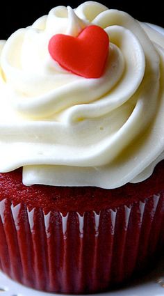 a cupcake with white frosting and a red heart on top