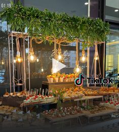 a buffet table filled with food in front of a store window at night and decorated with greenery