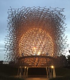 a large structure made out of sticks with lights on it's sides in the evening