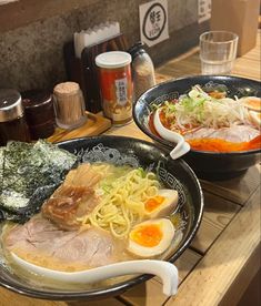 two bowls of ramen on a table with chopsticks and drinks in the background