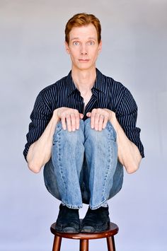 a man sitting on top of a stool with his legs crossed in front of him