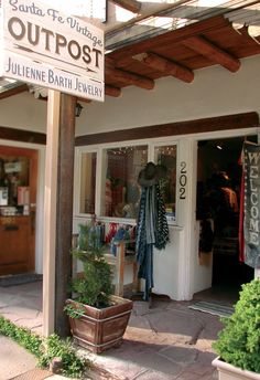 the outside of a clothing store with clothes on display and potted plants in front