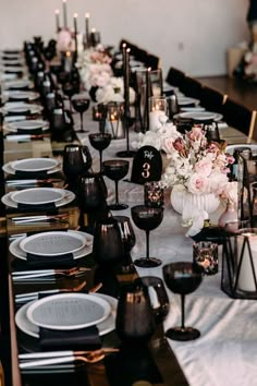 a long table is set with black and white plates, silverware, and flowers