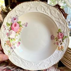 a white plate with pink and yellow flowers on it, being held up by someone's hand