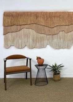 two chairs and a table in front of a wall hanging with fringes on it