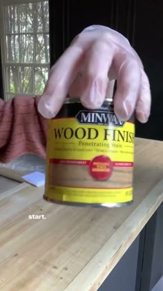 a person in white gloves is holding a can of wood finishings on a wooden table