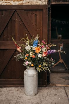 a vase filled with lots of flowers sitting on top of a cement floor next to a wooden door