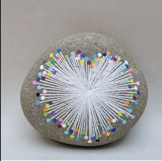 a rock painted with multicolored pins and thread on it's side, sitting on a white surface