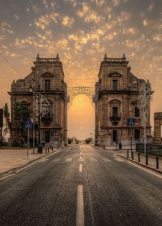 the sun is setting over an old building in front of a street with two gates