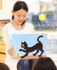 a woman holding up a cut out of a cat on a piece of paper in front of her