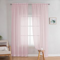 a living room with a chair, window and pink curtains in front of a white wall