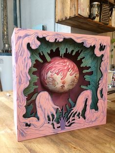 a pink and green box sitting on top of a wooden table next to a shelf