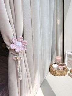 a pink flower is attached to the side of a white drapes in front of a window