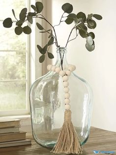 a vase with some plants in it on a table next to books and a window