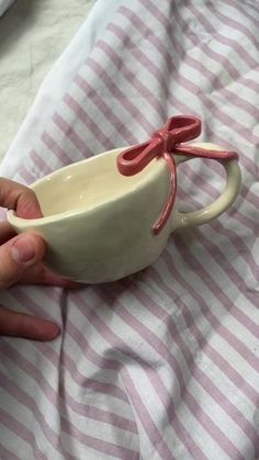 a hand holding a white and pink cup with a red bow on the handle that is attached to it