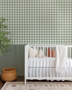 a white crib in front of a green checkered wall with a potted plant