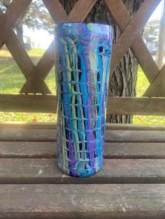 a blue vase sitting on top of a wooden bench next to a tree and fence