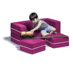 a young boy playing with a toy train on a purple couch that is shaped like a train track