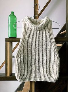 a white sweater hanging on a clothes rack next to a green bottle and stair case