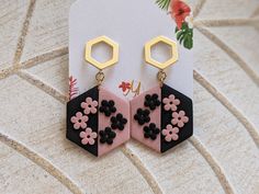 a pair of pink and black earrings with flowers on them sitting next to a card