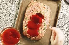 someone is spreading ketchup on top of a meatloaf with a spoon