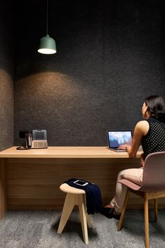 a woman sitting at a desk with a laptop computer on her lap and a lamp hanging from the ceiling