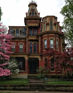 an old victorian style house with pink flowers on the front and trees in full bloom