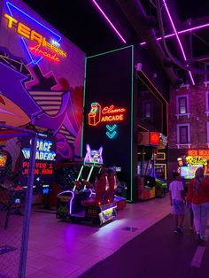 people walking through an arcade with neon signs on the walls and in front of them