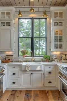 a kitchen with white cabinets and wooden floors, windows above the sink are lit by brass pendant lights