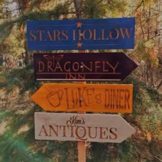 there are many different signs on the pole in the woods that read, stars hollow, dragonfly inn, duke's diner and antiques