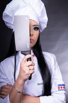 a woman with long black hair is holding a knife and looking at the camera while wearing a chef's hat