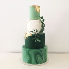 a three tiered green and gold wedding cake with greenery on the top layer