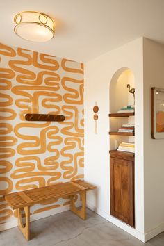 a wooden bench sitting in front of a wall with an orange design on it's side