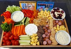 a tray filled with cheese, crackers and veggies next to other snacks