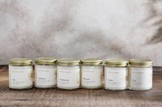 five jars of candles lined up on a wooden table